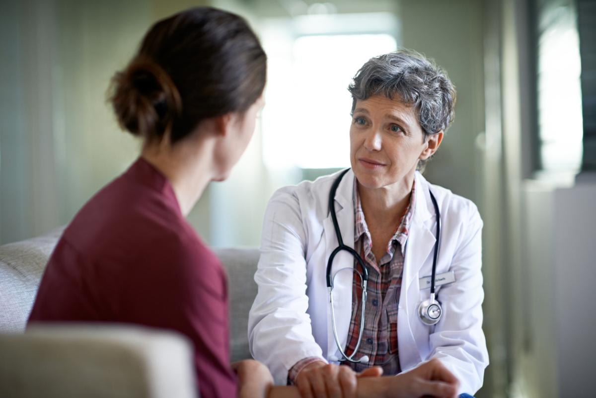 Female physician with short grey hair and a white coat consulting a female patient.