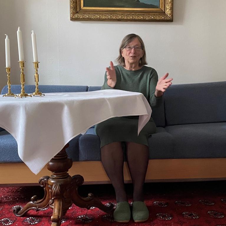 Charlotte Koren sittende i blå sofa ved et bord med hvit duk