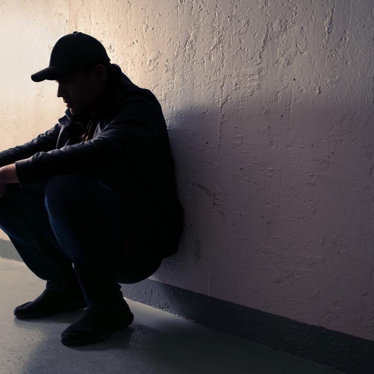 Mann sitter på huk inntil en vegg